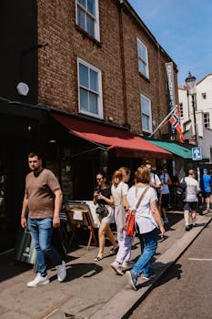 A vibrant street view of pedestrians walking along Portobello Road in London with a Norwegian flag visible.