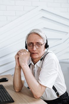 Portrait of a senior call center agent wearing glasses and a headset, engaged at work.